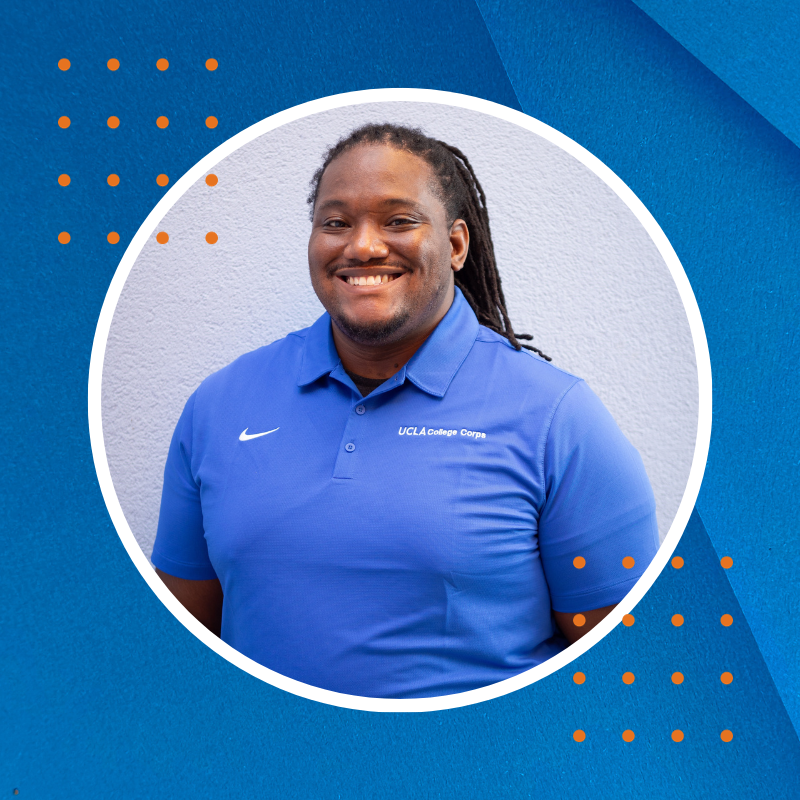 A smiling Black man, with long locs, in a blue shirt