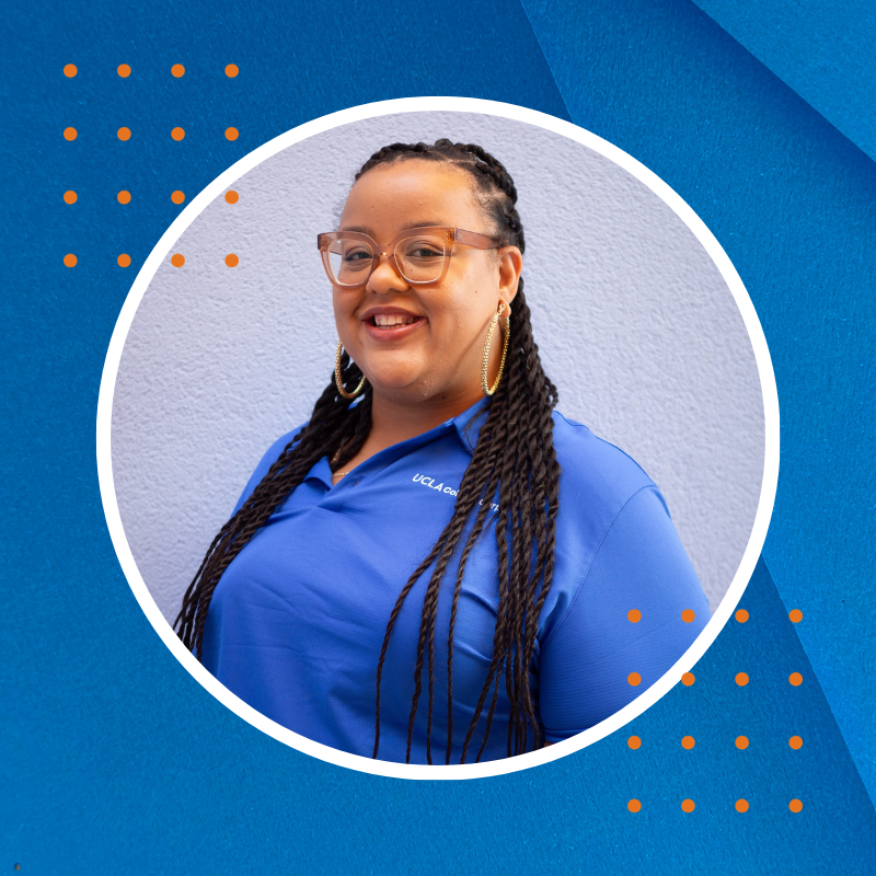 A smiling Black woman, with long black braids, and glasses, in a blue shirt