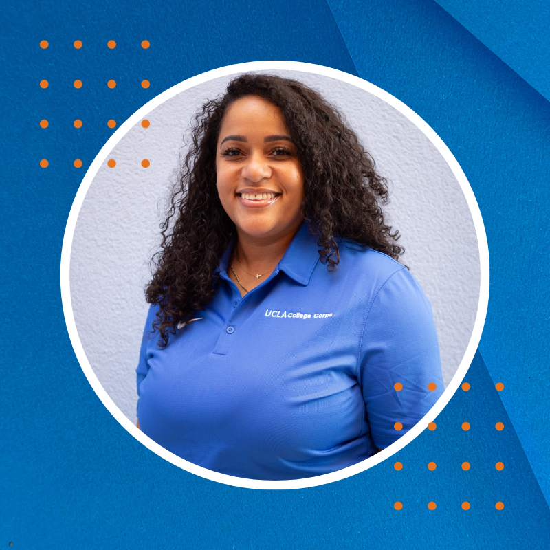 A smiling Black woman, with long curly hair, in a blue shirt